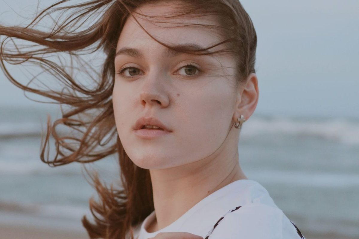 A woman at an Australian beach with her hair blowing in the sea breeze — summer hair care starts before you swim