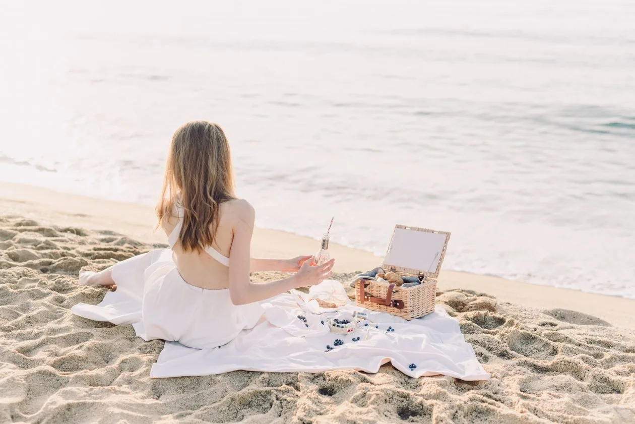 A woman enjoying a picnic with a wicker basket on a sunny Australian-style beach — summer Christmas gift inspiration for Mum