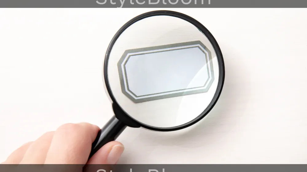 A hand holding a magnifying glass over a blank tag on a white surface.