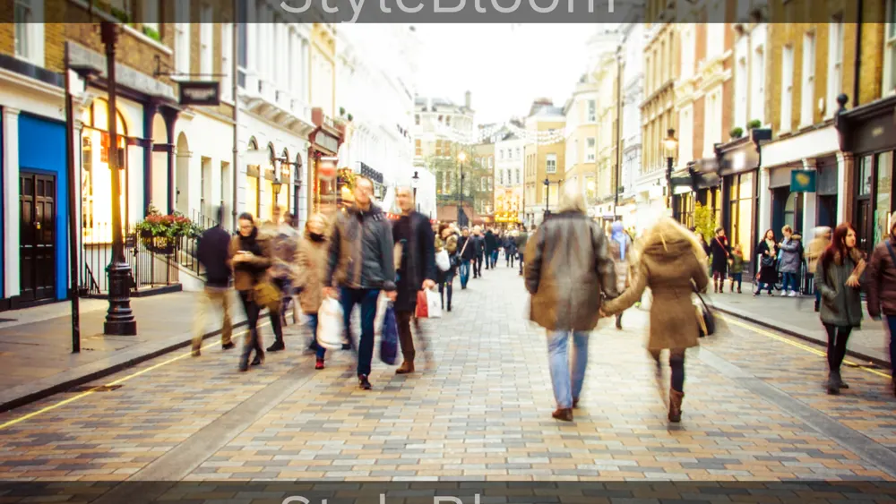 Shoppers in coats walking along a busy cobbled shopping street lined with shopfronts.