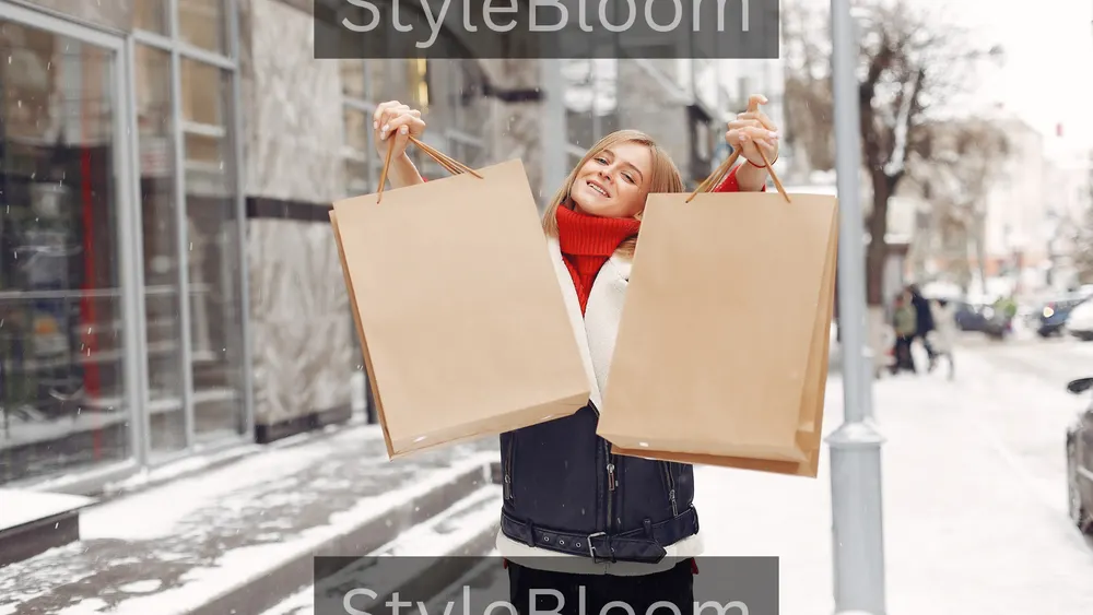 A woman in a red turtleneck holding two blank tan shopping bags on a snow-covered shopping street, with shopfront windows behind her.