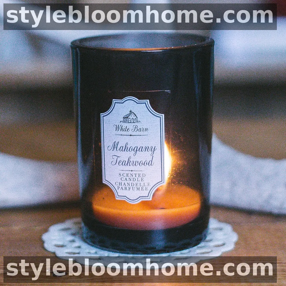 A lit mahogany teakwood scented candle in a dark glass jar on a wooden table