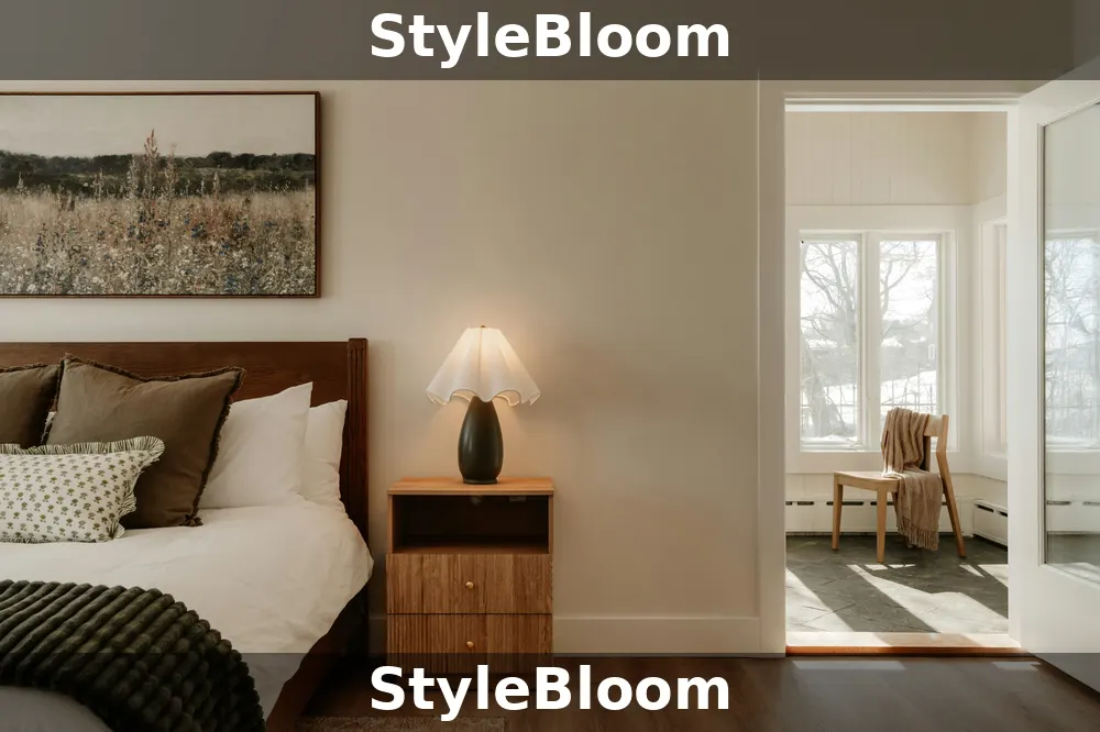 Made bed with layered pillows and a dark green throw, with a lit lamp on a wooden nightstand