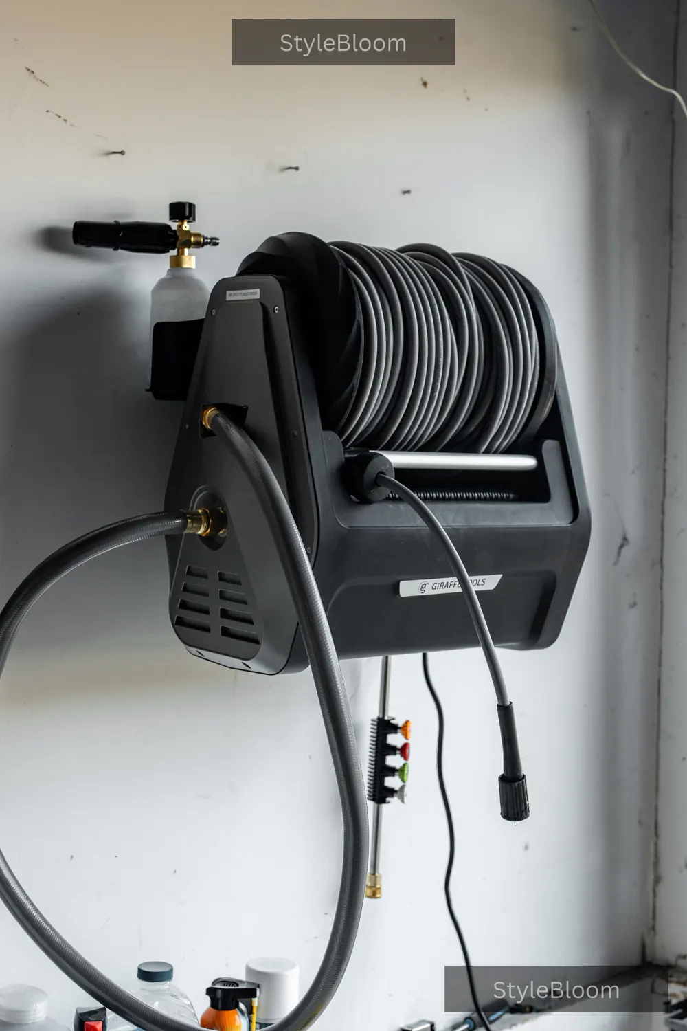 A wall-mounted pressure washer unit stored indoors — hose on its reel, foam cannon and nozzle tips together.