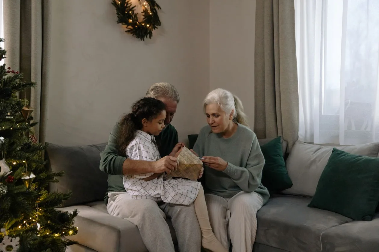 Grandparents opening a Christmas gift with their granddaughter by the tree — Christmas gift ideas for Nan
