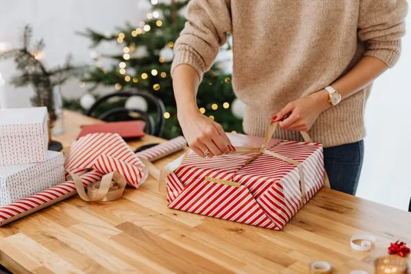 Hands wrapping Christmas gifts for Mum at a kitchen table — Christmas gift ideas for Mum in the UK